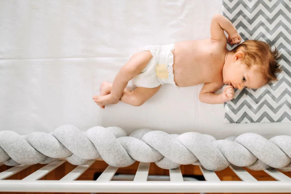bébé dans un lit vue du dessus avec un tour de lit grise en forme de tresse